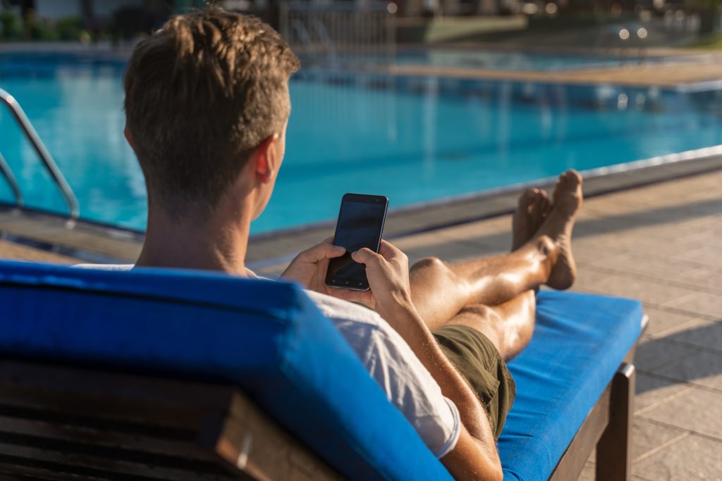 A man on loungechair checking phone by pool, to represent Men's Hair Trends Lowell.