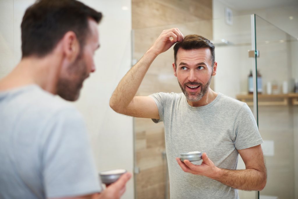Man applying hair gel to hair in bathroom, when searching for Men's Hair Stylists Near Downers Grove.