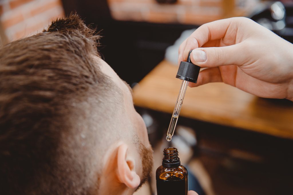 A barber applies tea tree oil to beard of client to represent Male Hair Care Oak Lawn.